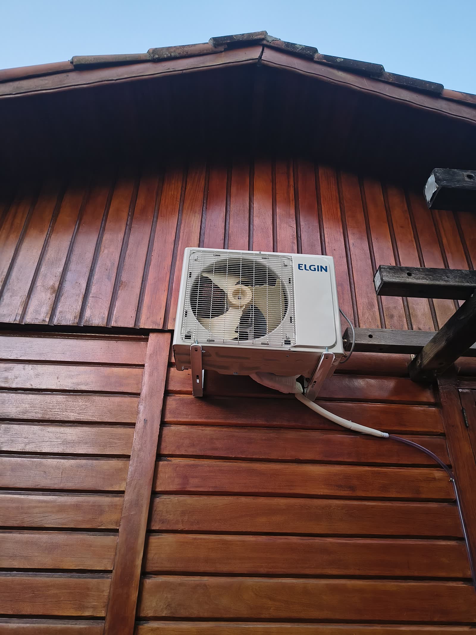 Condensadora Elgin fixada em suporte na fachada de madeira de uma casa, sob o beiral